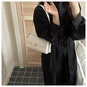 Gros plan d'un sac porté épaule blanc élégant avec serrure métallique et robe noire.