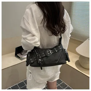 Detailed view of women black leather shoulder baguette bag with punk grommets and zippers.