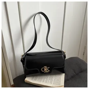 Détail de sac porté épaule en cuir vernis noir avec fermoir métallique et style minimaliste.