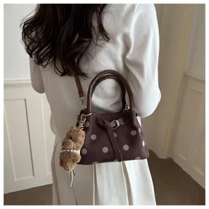 Gedetailleerd overzicht van bruine polkadot emmertas met leren riem en berenhanger.