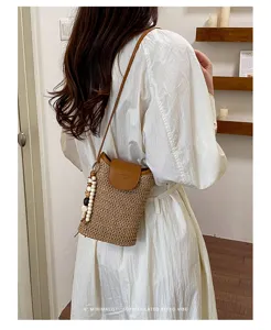 Detalle de bolso para teléfono de paja chic con solapa de cuero marrón y abalorios.