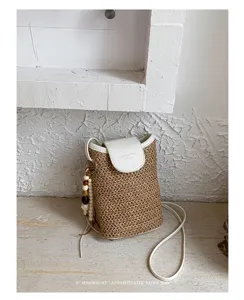 Detalle de primer plano del bolso de paja trenzada con solapa blanca y abalorios de madera.
