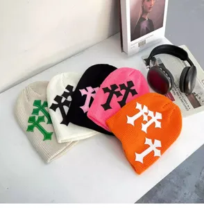 Vue détaillée de bonnets en tricot tendance avec patchs de croix, style streetwear hivernal.
