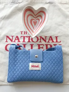 Close-up of blue knitted crossbody bag with diamond pattern, magnetic snap closure, and label.