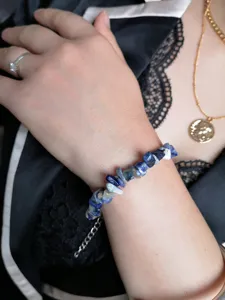 Primo piano di un bracciale di pietre naturali blu irregolari indossato al polso con catena.
