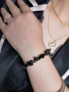 Dettaglio di un bracciale in pietra naturale nera irregolare indossato al polso elegante.