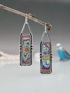 Primo piano di orecchini pendenti colorati in fordite stile boho pendono da un ramo d'albero.