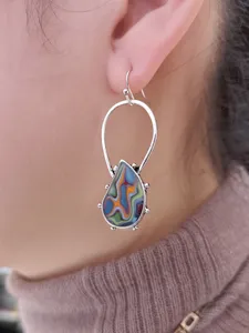Primo piano dettagliato di orecchini boho colorati a goccia con motivo a spirale artistico.