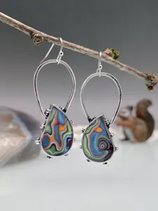 Primo piano di orecchini boho con motivi in pietra colorata vorticosa appesi al ramo.