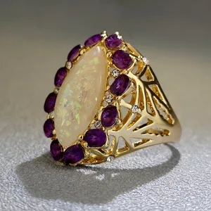 Dettaglio ravvicinato di anello dorato con grande opale e pietre viola di design.
