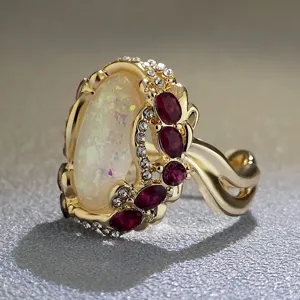 Primo piano dettagliato di un anello statement dorato con grande opale e pietre rosse.