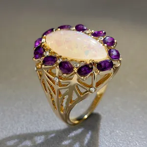 Dettaglio di un anello vintage dorato con un grande opale iridescente e pietre viola luminose.