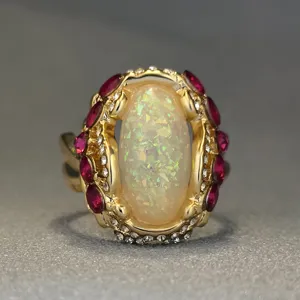 Anello con pietra opale centrale placcato in oro, pietre rosse e strass luminosi dettagliati.