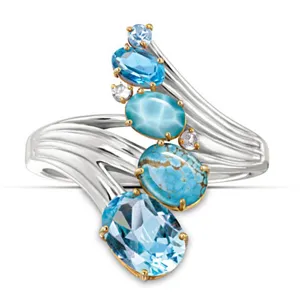Elegante anello con pietre preziose blu e design a onda in metallo argentato lucido.