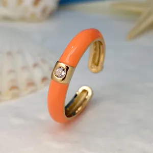 Primo piano di un anello aperto placcato in oro con smalto arancione vivido e cristallo.