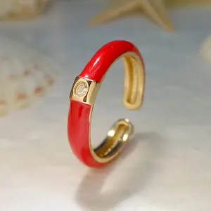 Primo piano di un anello aperto dorato con smalto rosso brillante e uno zircone luminoso.