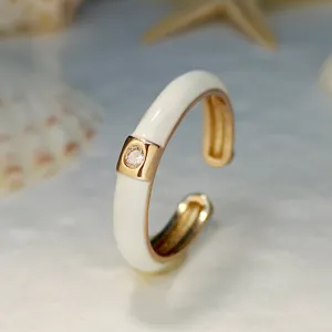 Dettaglio ravvicinato dell'anello aperto placcato in oro minimalista con smalto bianco.