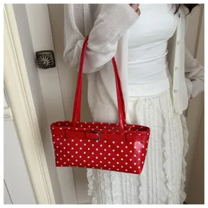 Detailed shot of the red polka dot patent leather shoulder handbag showing its unique belt buckle.