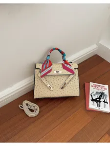 Detalle en primer plano de bolso Kelly beige con patrón de avestruz y pañuelo.