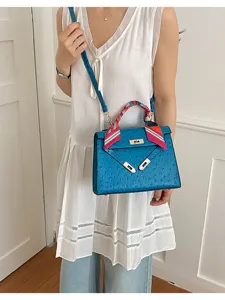 Detailed view of the blue ostrich texture Kelly handbag with chic scarf and metal lock design.