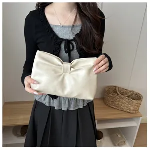 Detail view of cream faux leather bow clutch bag, showcasing unique gathered design and texture.