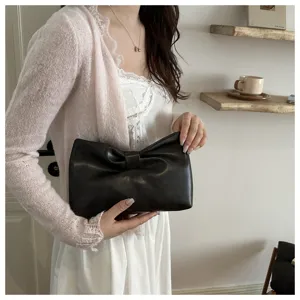 Close-up shot of the stylish black leather bow clutch bag, held by a model in interior setting.