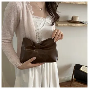 Detail shot of the dark brown leather bow clutch bag, showcasing stylish design and texture.