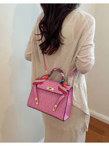 Pink ostrich texture Kelly handbag detail showing structured trapezoid design and twilly scarf.