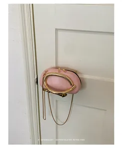 Detail view of pink round crossbody bag with unique gold ring handle and chain strap.