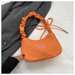 Vista dettagliata della borsa in nylon arancione con ricamo farfalla rosa e manico arricciato.