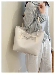 Glossy PU leather women's shoulder tote bag featuring a cute bow and heart pendant detail.