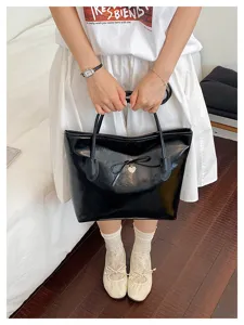 Classic black oil leather tote bag with bow and heart charm, retro minimalist design.