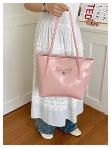 Pink leather tote bag detail showing cute bow and heart pendant in lifestyle setting.