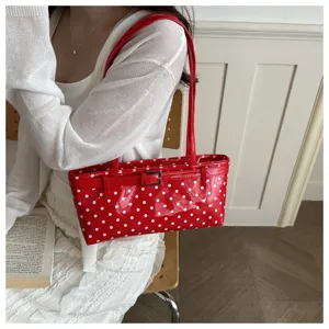 Close-up detail of the red polka dot patent shoulder bag, featuring a stylish belt buckle accent.