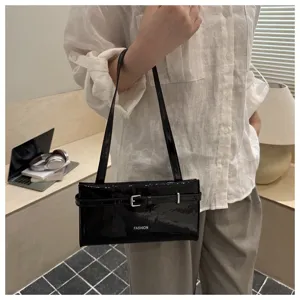 Detail shot of a black patent leather shoulder bag with a stylish belt buckle accent.