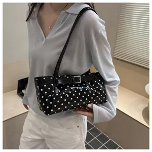 Closeup detail of chic black patent leather shoulder bag featuring classic white polka dots.