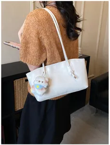 Detailed view of white shoulder tote bag with cute plush pendant, fashion daily lifestyle shot.