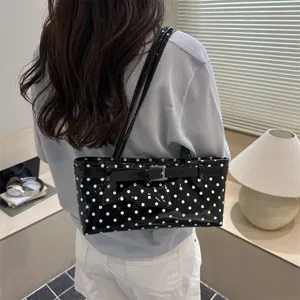 Black patent leather shoulder bag with white polka dots, chic belt buckle strap, trendy design.