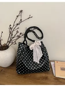 Elegante bolso de hombro negro de lunares con asas trenzadas y bonito lazo rosa tierno.