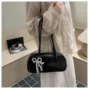 Primer plano de bolso de hombro de cuero negro con elegante colgante de lazo de perlas y asas.