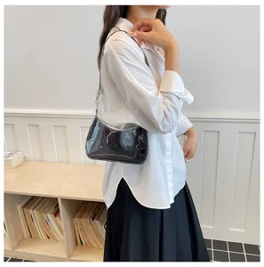 Detailansicht einer stilvollen schwarzen Lackleder-Schultertasche, lässig von Model getragen.