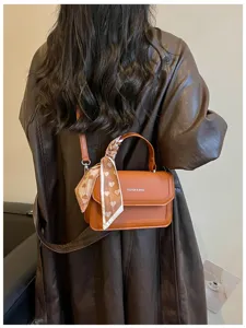 Gros plan détaillé du sac à bandoulière en cuir PU marron avec un foulard en soie noué.