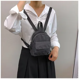 Close-up view of the dark plaid mini backpack worn by the model, showing front pocket detail.
