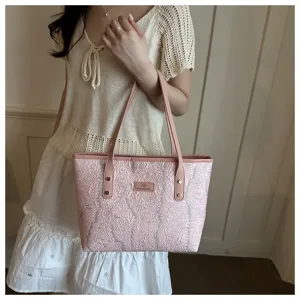 Detailed view of the pink textured tote bag with shoulder straps and chic front logo badge.