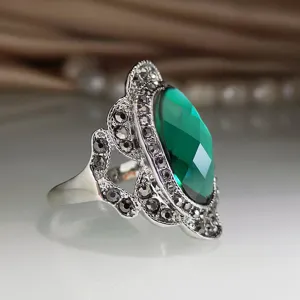 Detailopname van vintage zilveren ring versierd met grote groene edelsteen en steentjes.