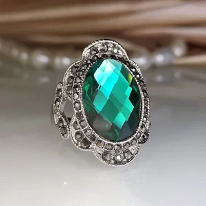 Vintage groene edelsteen ring met sprankelende kristallen en zilverkleurige band.