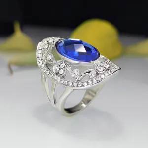 Detailopname van de zilverkleurige opengewerkte ring met grote blauwe kristal en steentjes.