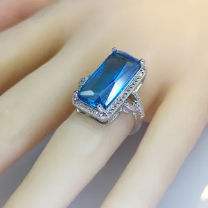Stunning emerald-cut blue gemstone ring with pave-set rhinestones and split shank design.