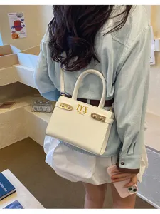 Detail view of stylish white shoulder handbag with golden hardware and letter print in cafe scene.