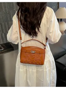 Brown leather shoulder bag with embossed hearts and metal lock detail, stylish accessory.